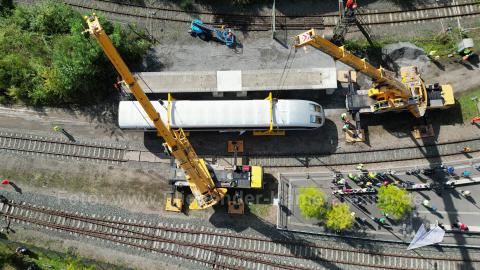 Luftaufnahme der Drohne bei Sonnenschein: Der Transrapid wird von zwei mobilen Kränen gehalten.